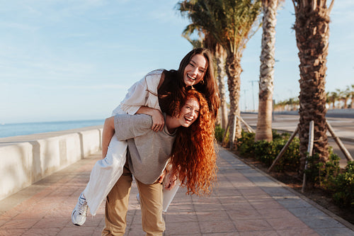 Energetic young woman piggybacking her best friend in the promen