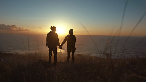 Traveling couple on cliff at sunset.