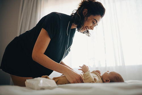 Mother smiles as she changes baby's diaper at home