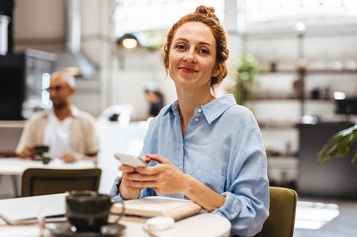 Postgrad student using smartphone while studying in coffee shop