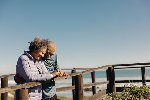 Happy senior couple smiling while standing on a foot bridge at the beach