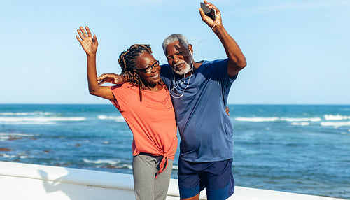 Mature couple dancing and celebrating by the coast in exercise gear