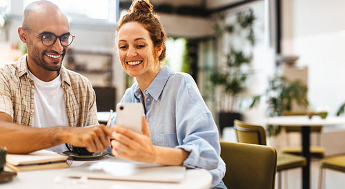Happy colleagues using a mobile phone while working together in a cafe
