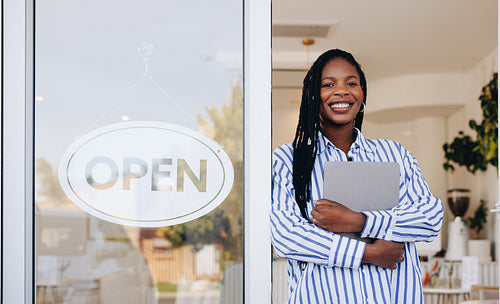 Happy young coffee shop owner standing at the doorway of her newly opened coffee shop