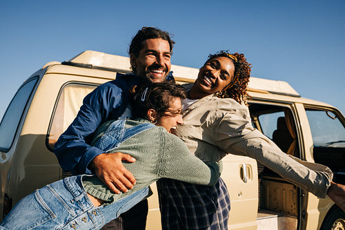 Friends embrace beside a beige van on a sunny day