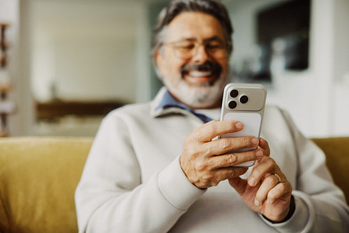 Senior man uses a smartphone while relaxing on a sofa