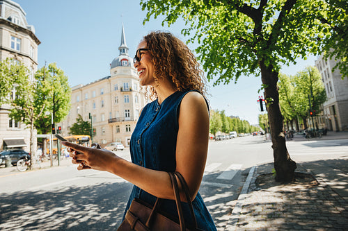 Woman waits for ride using a smartphone on a sunny urban street
