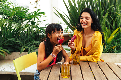 Mother and daughter enjoying fruit popsicles together outdoors in a garden setting