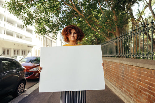Confident teenage girl holding a blank white placard in the city