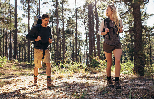 Hiking couple walking in forest wearing backpacks
