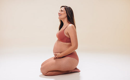 Expecting mother embracing her baby bump with a radiant smile in a studio setting