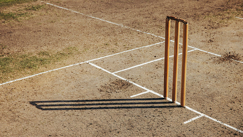 Wooden cricket stumps on a dry field with marked pitch lines
