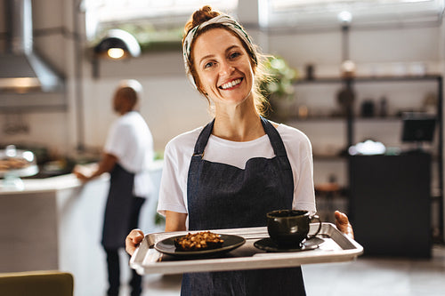 Portrait of a happy waitress holding a tray of food in a coffee