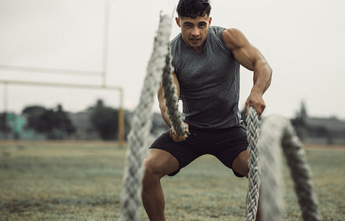 Muscular man working out with battling ropes