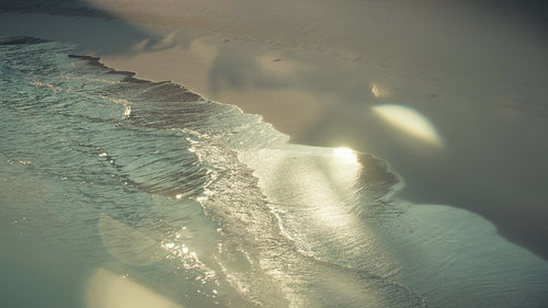 Golden morning light over gentle tropical ocean waves and sandy beach