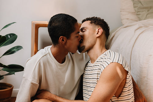 A young gay couple sharing a loving kiss in a cozy room