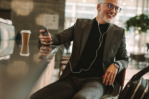 Mature man at coffee shop listening music from phone