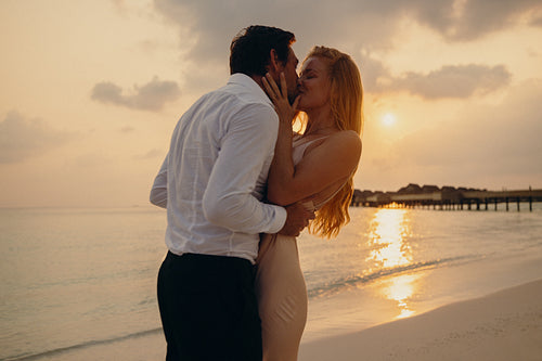 Dreamy honeymoon moment of a couple kissing on a beautiful beach at sunset