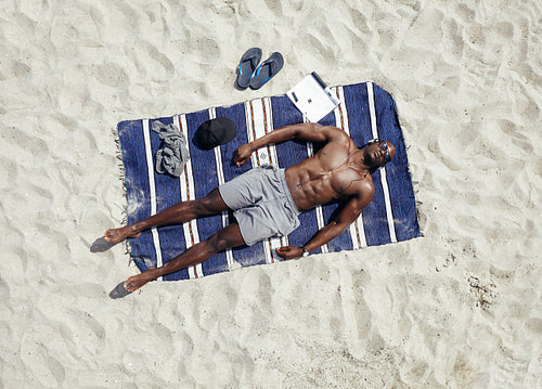 Young guy lying shirtless on a mat sunbathing