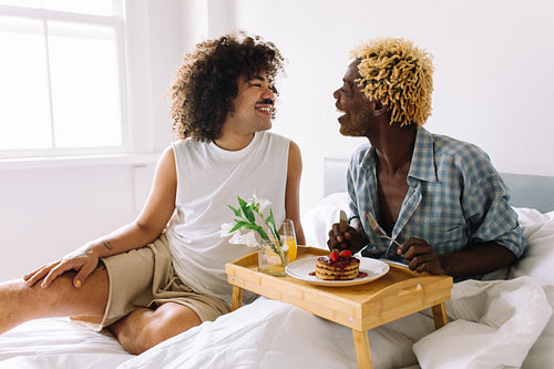 Young gay man eating breakfast in bed