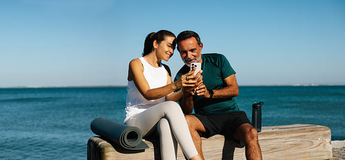 Middle-aged couple enjoying time together by the sea while on mobile device