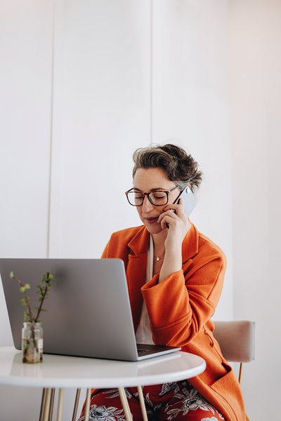 Businesswoman speaking on a phone call while working on a laptop in a cafe