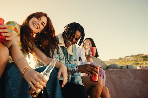 Happy young friends laughing and enjoying drinks outdoors on a sunny day