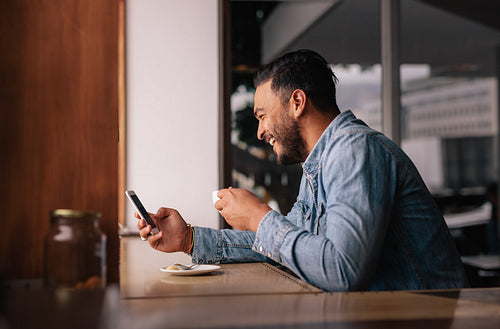 Handsome guy at cafe using smart phone and having coffee