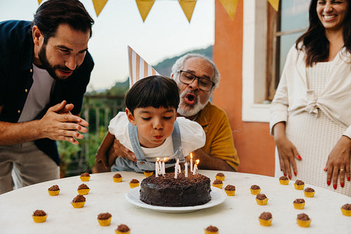 Child blowing out birthday candles with father and grandfather cheering