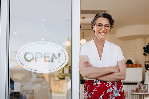 Friendly cafe owner smiling at the camera while standing at the entrance of her newly opened shop