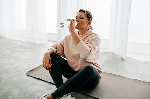 Fitness recovery begins as the woman drinks water on her yoga mat indoors