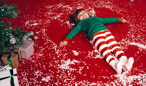Kid lying down on floor beside a christmas tree