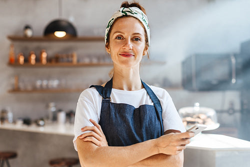 Woman in an apron stands in her coffee bar, holding a smartphone