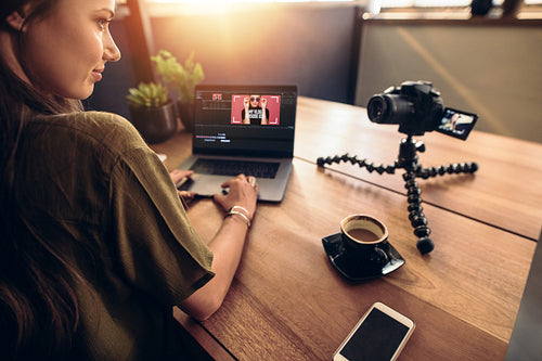 Young female vlogger looking at her camera while editing her vlog on computer.