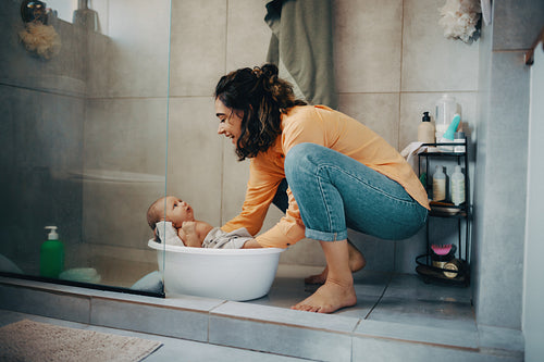 Mother bathes baby in tub at home, smiling