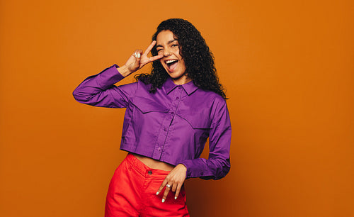 Happy woman with stylish fashionable curly hair making a peace sign gesture on a colored background
