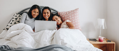 Girls watching a movie on laptop lying on bed