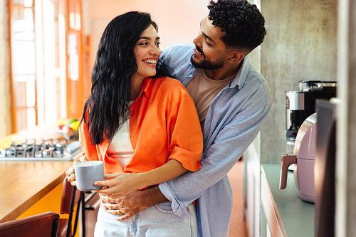 Happy couple embracing in bright kitchen while enjoying morning coffee