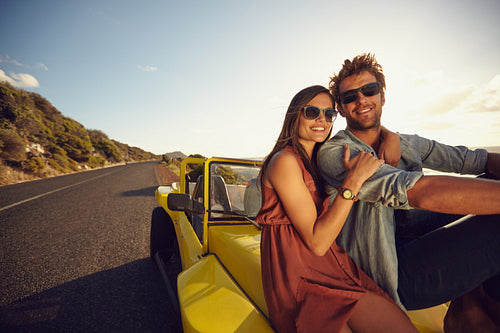 Attractive young couple sitting on the hood of their car