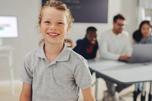 Young school boy smiling at the camera in a coding class, with his classmates in the background