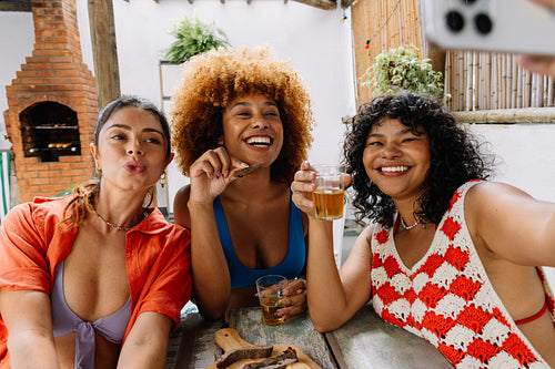 Three friends smiling and taking a selfie during Brazilian churrasco gathering