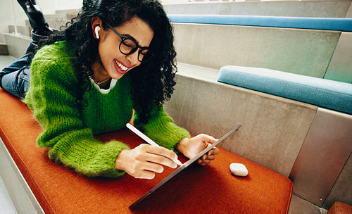 Woman using tablet for creative work in public library with stylus and headphones