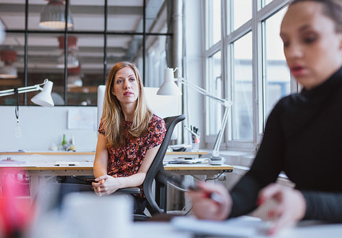 Young woman sitting at her desk looking away thinking