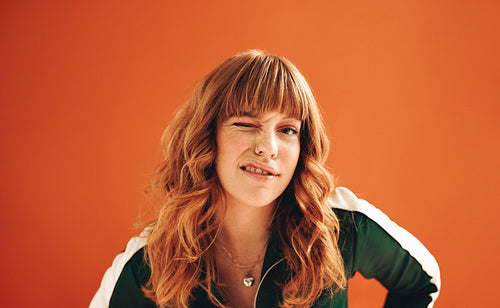 Quirky young woman winking at the camera while standing in a studio