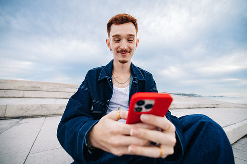 Young man smiling while using smartphone outdoors