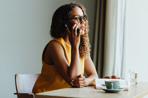 Woman in cafe talking on cellphone with notebook and coffee