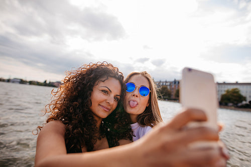 Teenage girls taking selfie with smart phone by the lake