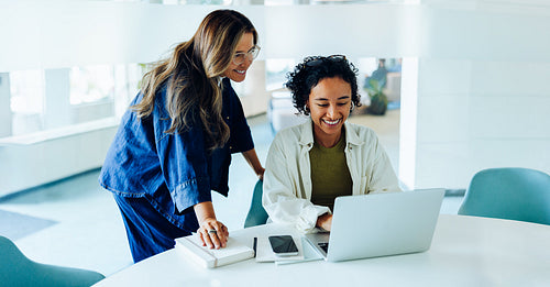 Two women guide one another at laptop