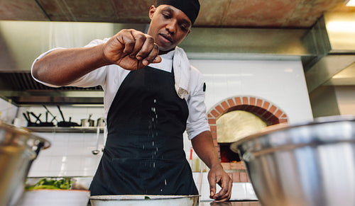 Chef sprinkling spices on dish in commercial kitchen