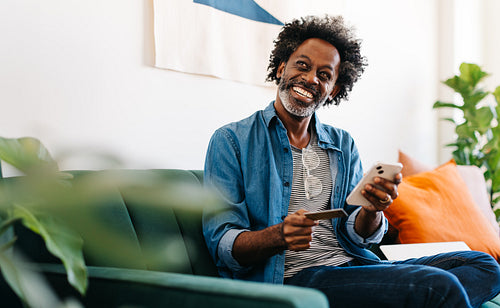 Happy mature man smiling and enjoying online shopping on his smartphone at home